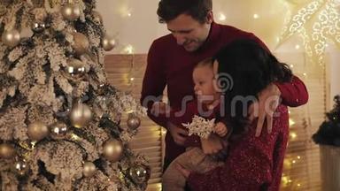 幸福的微笑家庭与小宝宝站在圣诞树附近舒适的客厅，妈妈抱和拥抱宝宝，丈夫